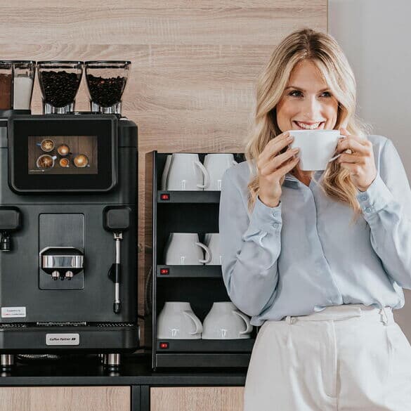 Frau-steht-mit-tasse-vor-kaffeebar-mit-barista-ultima