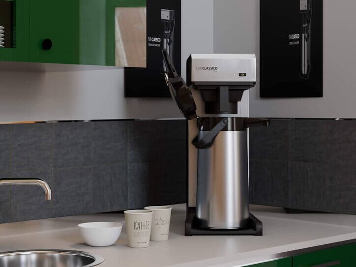 Filterkaffeemaschine auf einer Küchenarbeitsplatte, umgeben von grünen Schränken und schwarzer Fliesenrückwand.