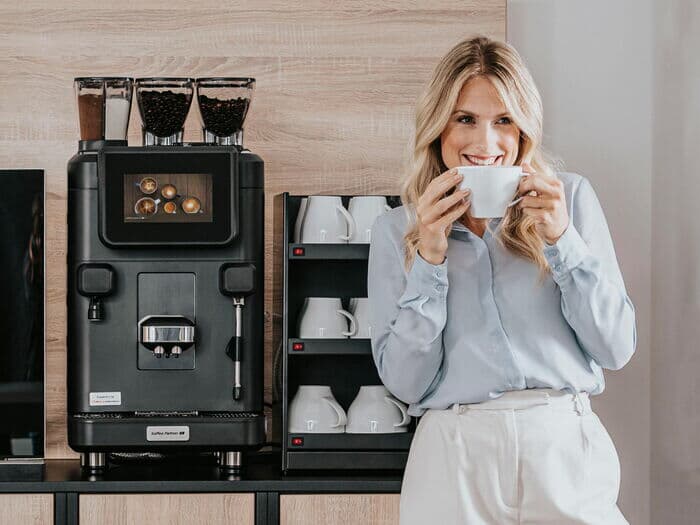 Frau-steht-mit-tasse-vor-kaffeebar-mit-barista-ultima